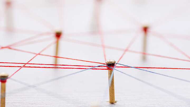 Plansza z wbitymi spilkami do których przywiązano czerwone nici symbolizujące sieć.